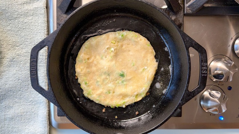 Scallion pancake cooking in oil in cast iron skillet