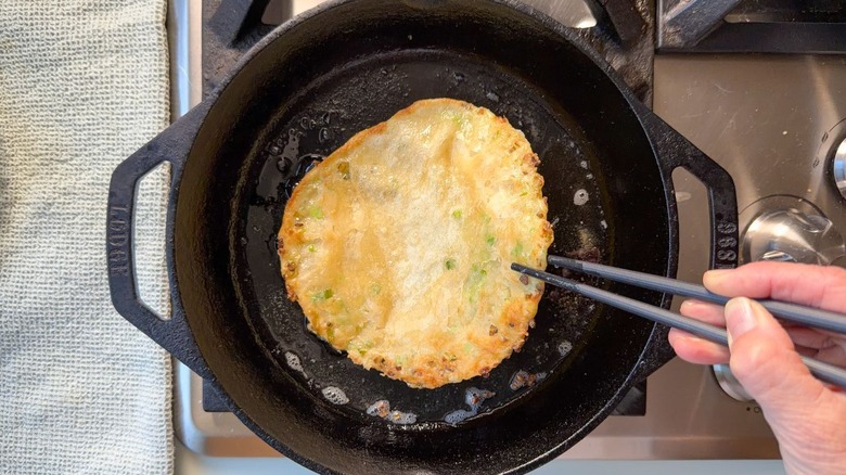 Flipping scallion pancake in cast iron skillet with chopsticks