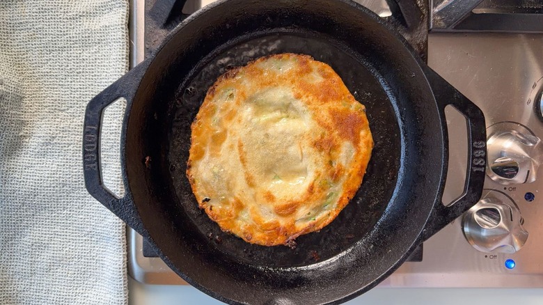 Crispy scallion pancake cooking in cast iron skillet