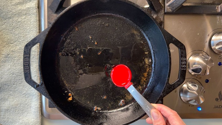 Adding peanut oil to cast iron skillet with tablespoon measure