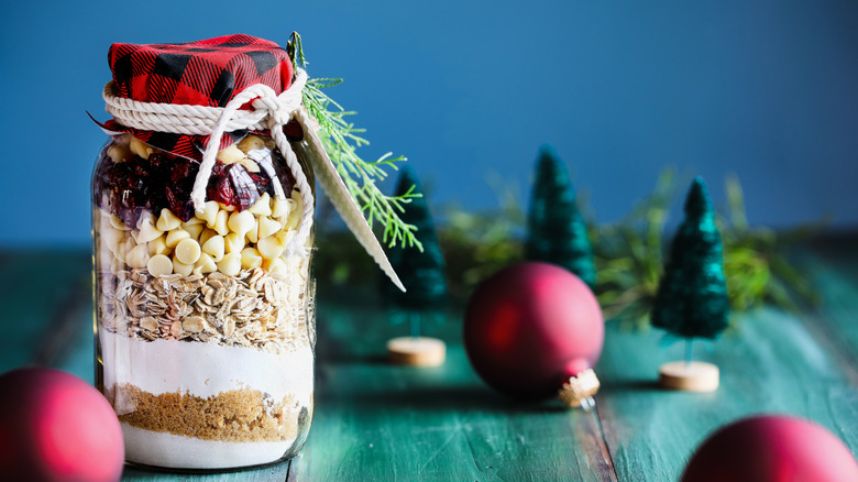 A holiday mason jar with layered cookie mix on festive table with ornaments
