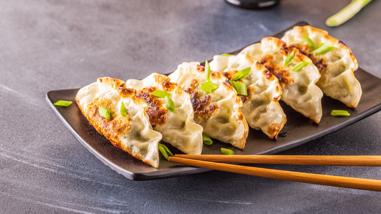 Tray of crispy potstickers with green onions and chopsticks
