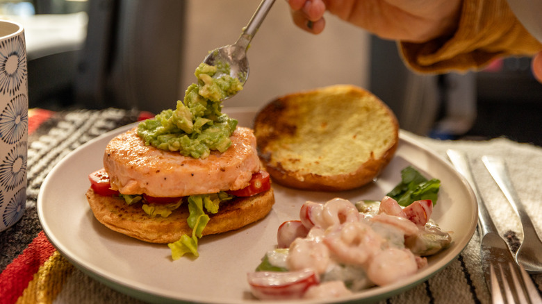 Salmon burger with avocado being spooned on top of the patty