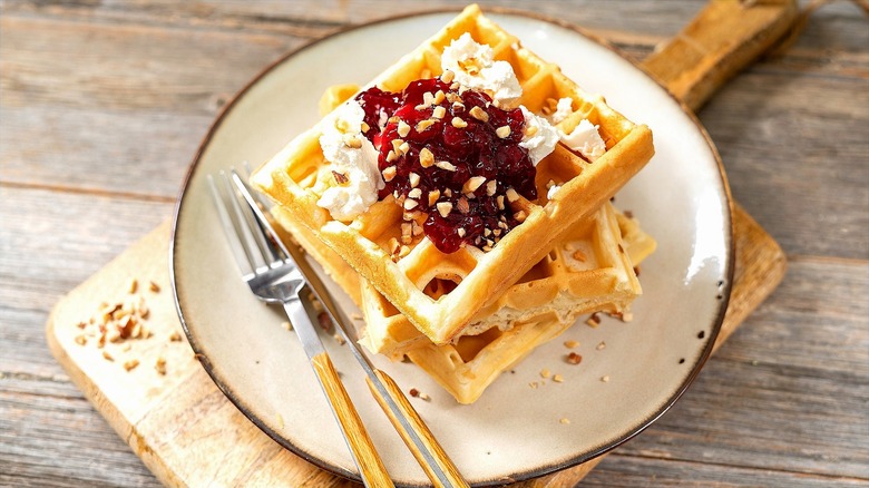 Stacked waffles on a plate with Greek yogurt, jam, and crushed nuts