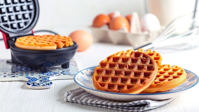 Waffle in waffle iron and stack of waffles on a blue and white plate