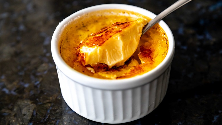 Spoon scooping crème brûlée out of a white ramekin