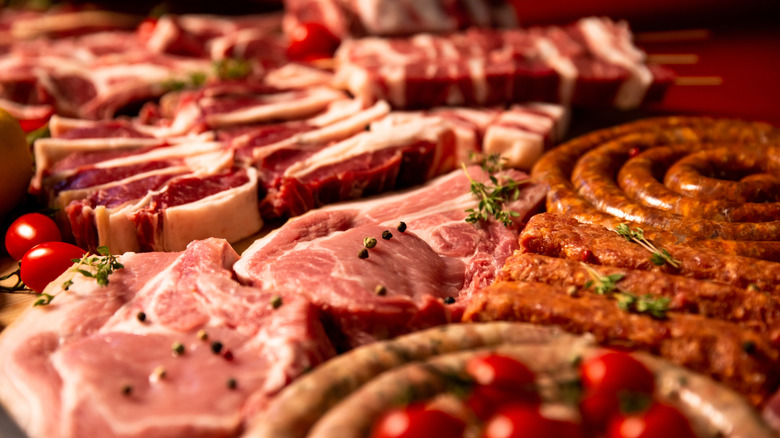 Various preparations and cuts of raw meats and sausages with tomatoes scattered around