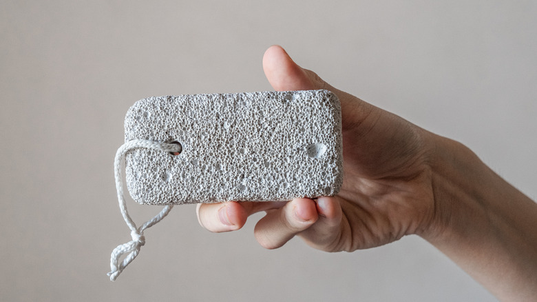 A close-up of a hand holding a pumice stone against a light gray background