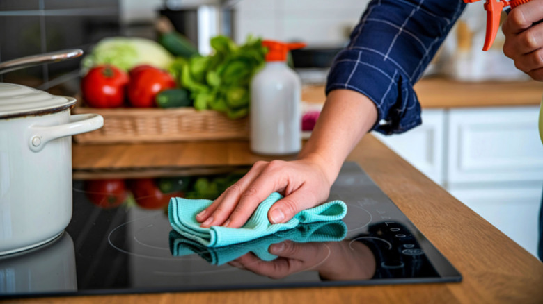 A close-up of a hand wiping dirt and grime away from the stovetop with a soft cloth.