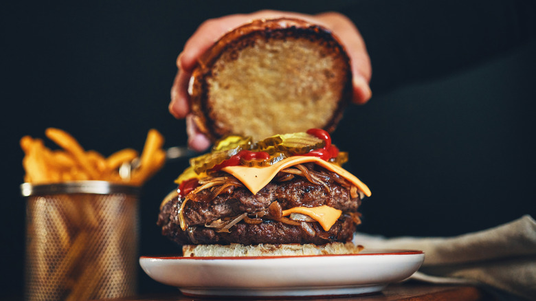 Putting the top bun on a burger with cheese, pickles, and onions