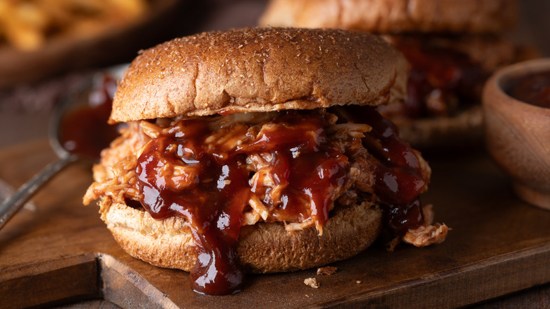 Close up of BBQ shredded chicken on wheat bun on cutting board