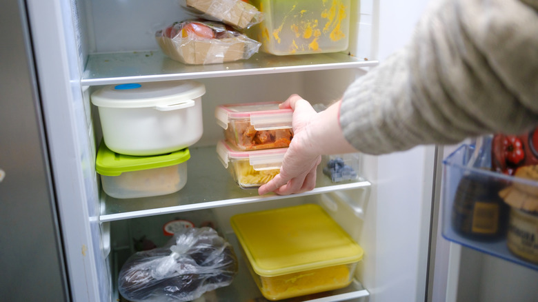 An individual refrigerating cooked pasta and chicken leftovers.