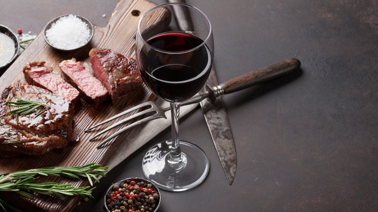 A glass of red wine is arranged beside a steak sliced on a cutting board