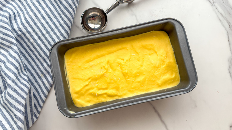 Mango ice cream in loaf pan next to ice cream scoop