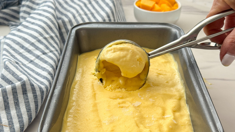 hand scooping mango ice cream from loaf pan