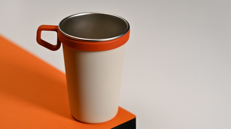 Gray cup with orange plastic cup holder on an orange table.