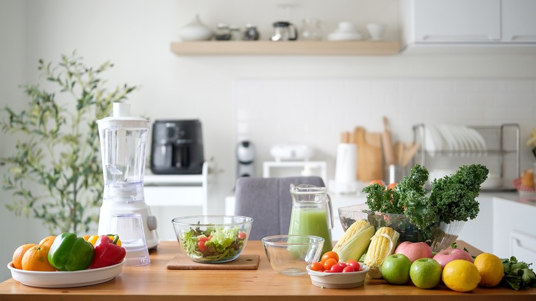 a cluttered kitchen countertop with fruits, vegetables, bowls, and a blender