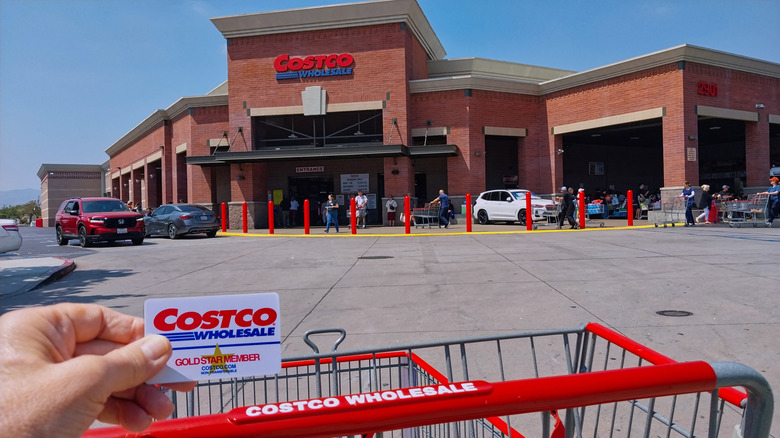 Person holding a Costco card over a cart outside a Costco store