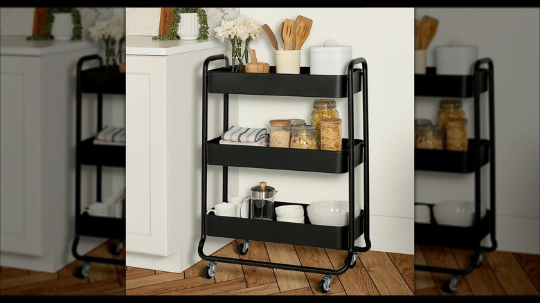 An assembled black kitchen cart with jars of food, utensils, and flowers