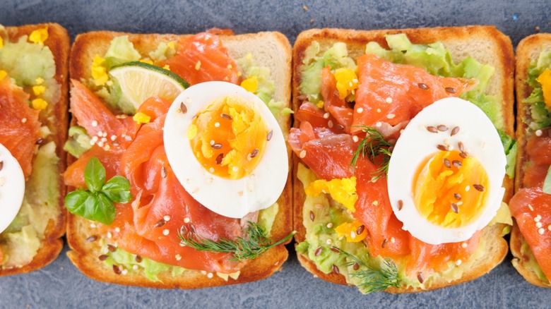 Avocado toast with smoked salmon and a boiled egg garnished with dill, sesame seeds and lime