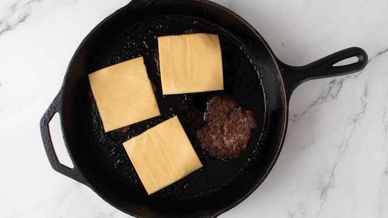 Burgers topped with cheese in cast iron skillet