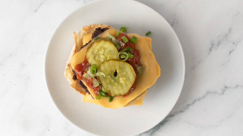 Uncapped cheeseburger with pickles, scallions, and sauce