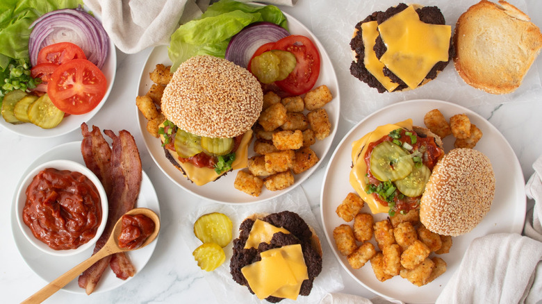 Various smash burgers with tater tots, burger toppings, and sauce