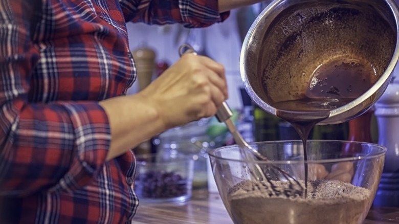 A person pouring brownie batter from a bowl into a baking sheet.