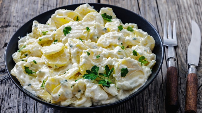 Bowl of creamy potato salad with a fork and knife on the side