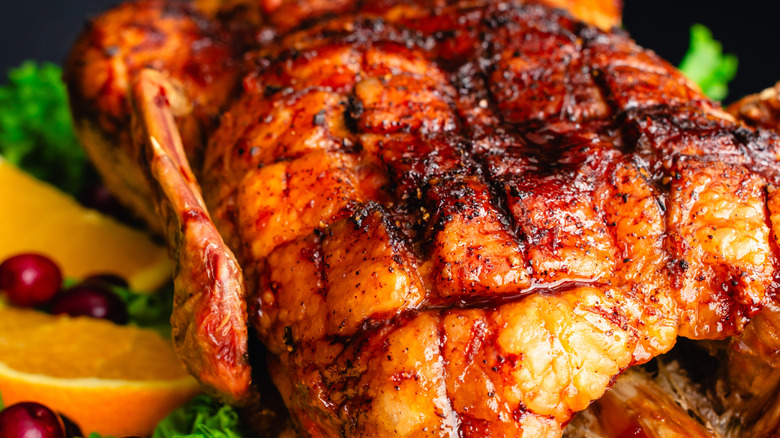 Glazed whole duck next to fresh oranges and cranberries