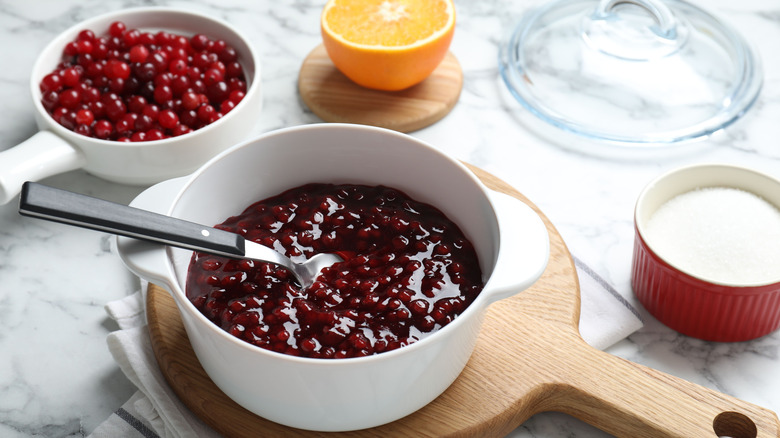 Cranberry glaze in bowl on wood cutting board with fresh cranberries and orange in background