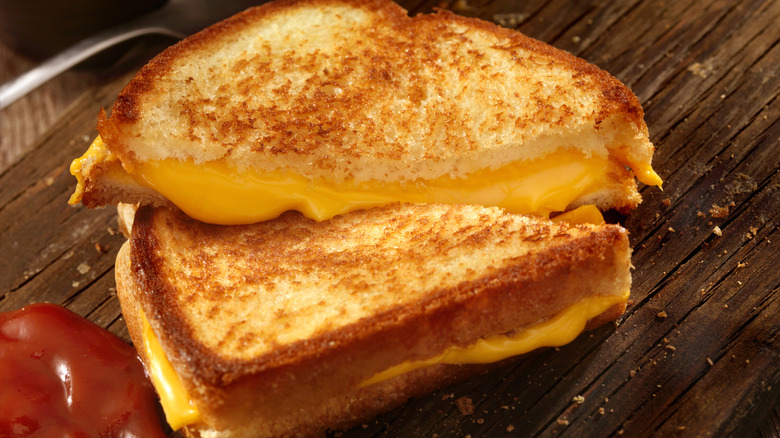A gooey grilled cheese sandwich on a wooden cutting board.