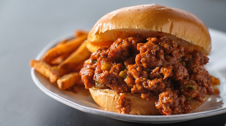 Sloppy joe on white plate served with fries.