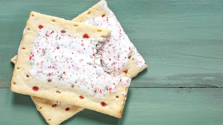 Two frosted strawberry Pop-Tarts layered on top of one another on a green wooden surface