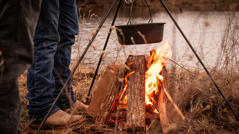 A pot over a campfire with a cowboy standing nearby.