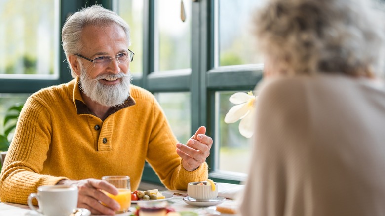 Smiling older couple sitting at a restaurant table chatting and nibbling on breakfast