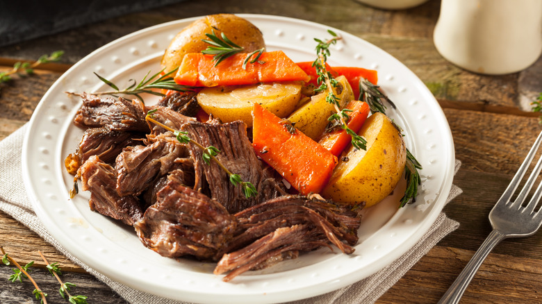 A plate containing pieces of beef, potatoes, and carrots garnished with fresh herbs