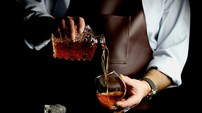 A person pouring dark liquor from a decanter into a glass.