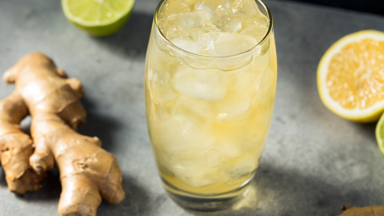 a glass of ginger ale with ice on a table with ginger root and lemons