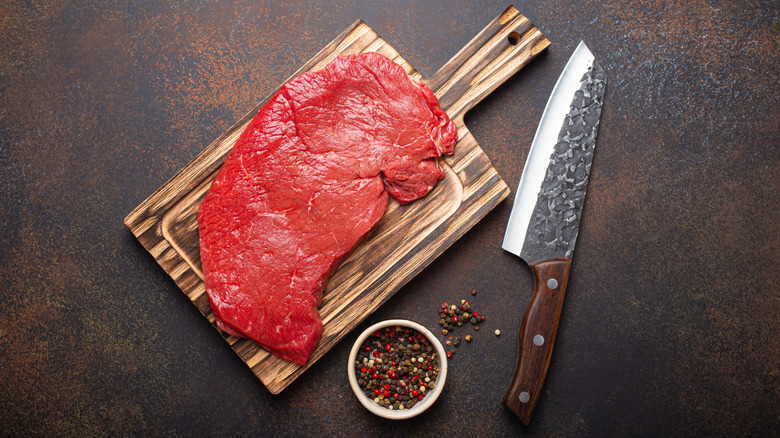 Top round steak on a cutting board with a knife and spices