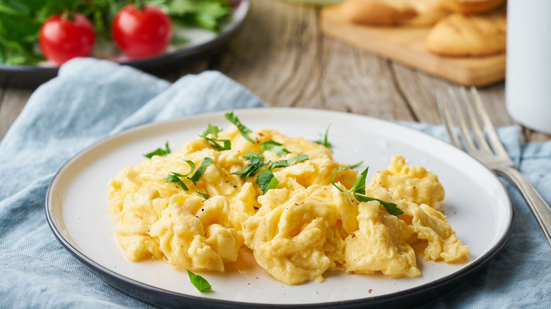 scrambled eggs on a white plate with fresh tomatoes