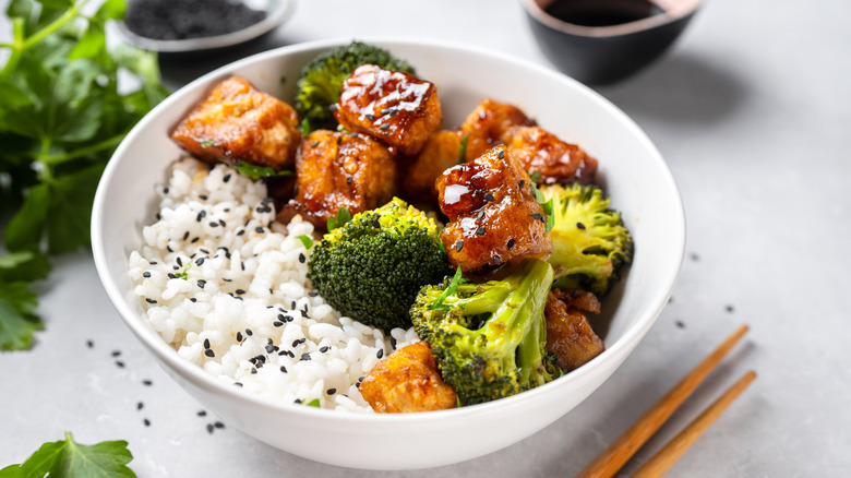 broccoli and tofu rice bowl with black sesame garnish and chopsticks nearby