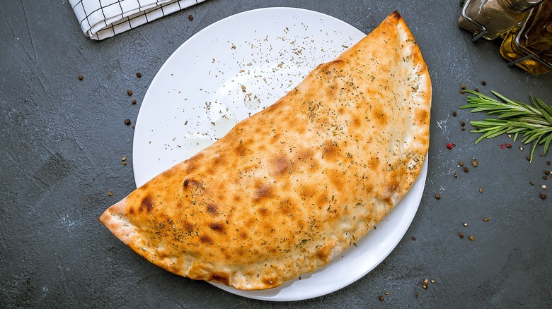 Large baked calzone with dried herbs on a white plate