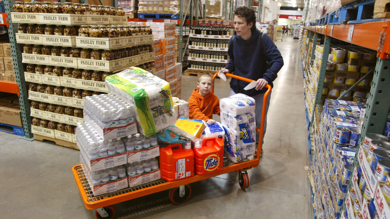 A Costco shopper with a pile of products on a shopping trolley.