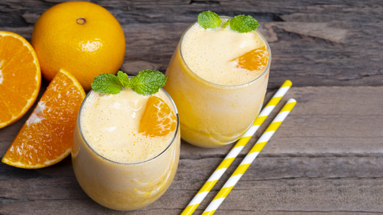 Two glasses of orange smoothies next to straws and sliced oranges