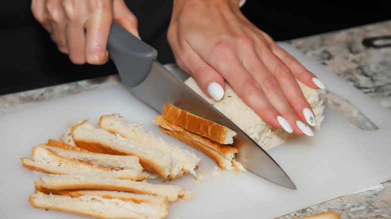 Person with a white manicure cutting the crust off a white bread sandwich