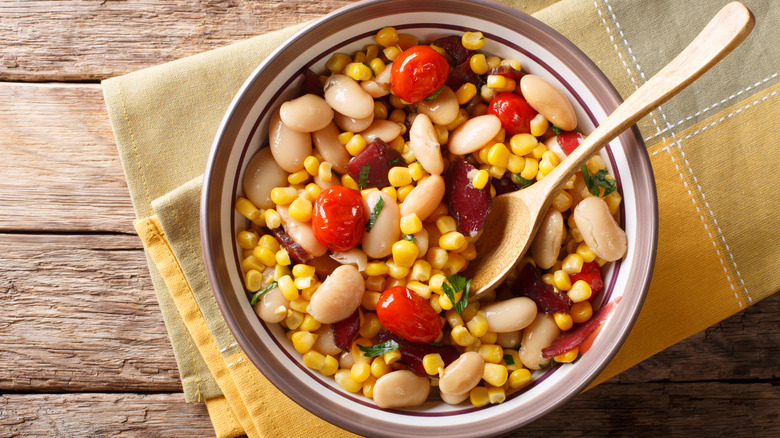 A bowl of succotash with corn, lima beans, and tomatoes on a wooden table.