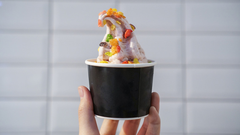 A person's hand is seen holding a cup of frozen yogurt topped with cereal.