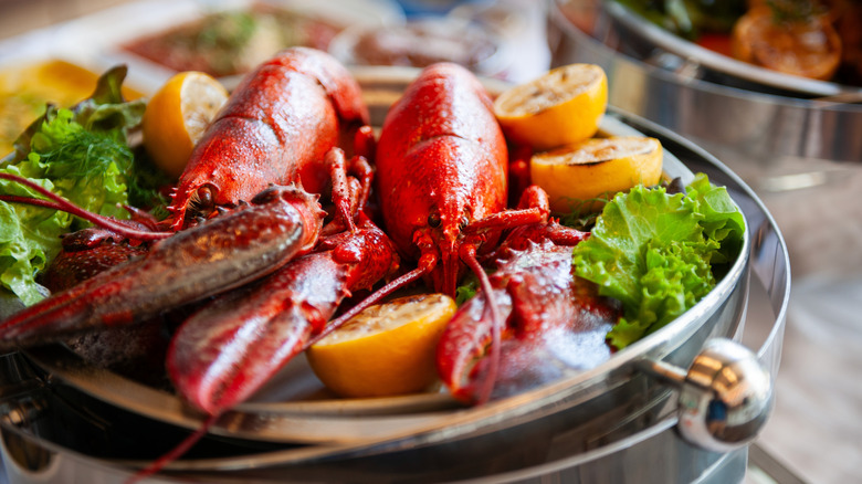 Two bright red lobsters are plated with lemon halves.