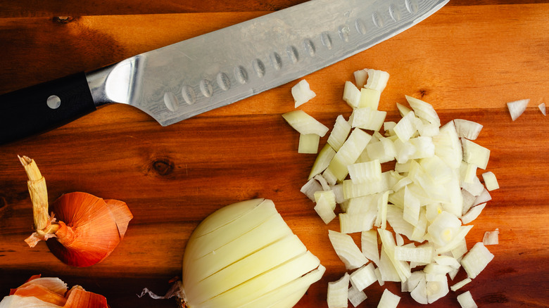 Chef's knife on a chopping board with diced onions